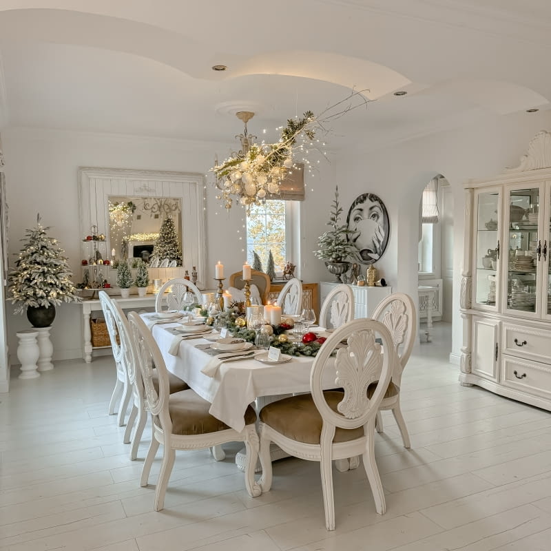 Warto zadbać o spójną aranżację całej jadalni. Tutaj wszystko utrzymane jest w bieli, nawet drzewka są delikatnie pobielone. Czerwień pojawia się tylko w detalach.