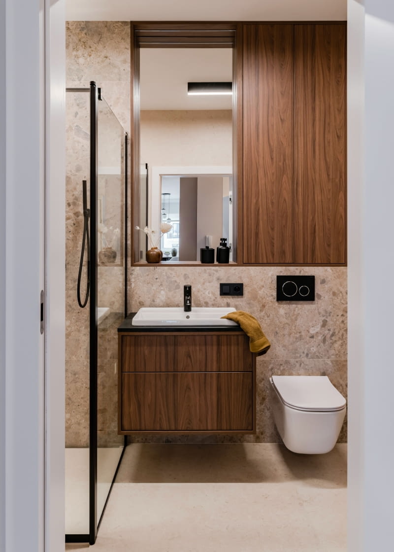 Wystrój łazienki stanowi harmonijną kontynuację stylistyki całego mieszkania. Dominują tu beże i brązy, ożywione czernią. Wyraziste płytki na ścianie z umywalką i prysznicem  to włoskie Marazzi Caracter Mix Multicolor o fakturze imitującej kamień.