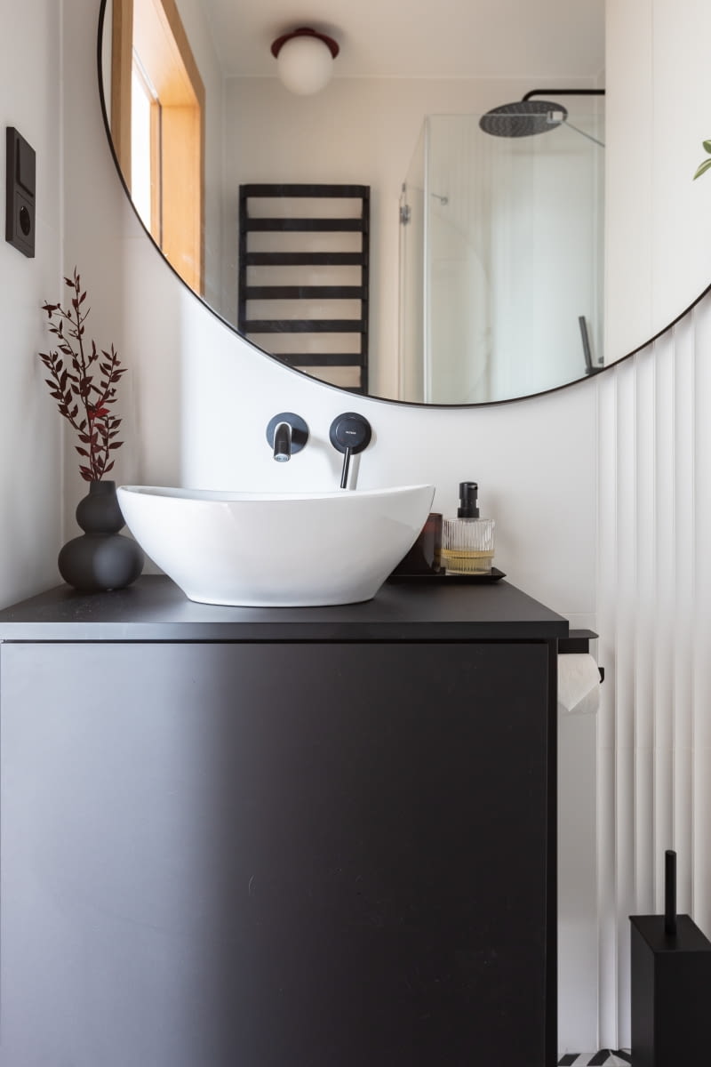 Czarna szafka pod umywalką, a także czarne, ażurowe półki zamontowane na tle białego, ryflowanego panelu Orac oraz zabudowa meblowa nad stelażem WC powstały w pracowni stolarskiej Płuciennik.
