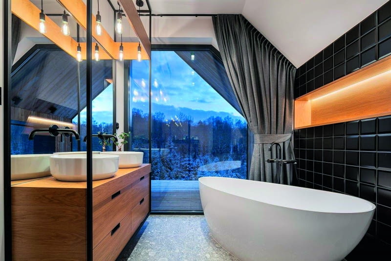 Kąpać się czy może jednak podziwiać niezwykłe widoki „wyświetlane" przez naturę na dużym oknie – albo wyjść na głęboki i rozległy taras schowany  pod dwuspadowym dachem górnej kondygnacji? W razie kłopotów z nadmiarem bodźców wystarczy uwolnić masywne zasłony i znajdujemy się  z powrotem sam na sam w łazience, odciętej od „teatrum" świata, pełnej dobrze pomyślanego sztucznego światła, z ciepłą wodą w wannie...