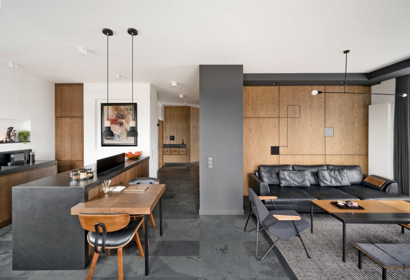 Ciemne barwy drewna i kamieni wprowadzają przyjemny nastrój wyciszenia i relaksu. We wnętrzu dominują naturalne materiały: łupek, granit, marmur, lniane tkaniny, tapety z plecionek oraz najważniejszy element – drewno w różnych odcieniach i odmianach. Czarna, skórzana sofa została uszyta według projektu Marty. Wykonał ją tapicer Marek Jaworek z firmy Rafek Meble w Starych Babicach. Fotele o ciekawej konstrukcji z giętego pręta stalowego pochodzą od marki Prostoria. A skromną lampę wiszącą nad kącikiem wypoczynkowych kupiono w Elmax’ie.