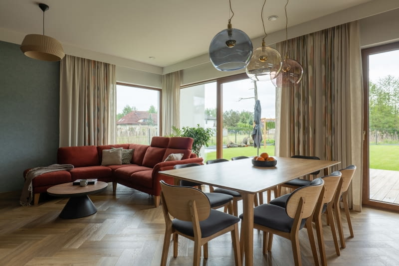 W strefie dziennej zastosowano duże, wielkoformatowe przeszklenia, które otwierają wnętrze na taras i ogród. Dzięki nim dom płynnie łączy się z otoczeniem, z czego rodzina chętnie korzysta na co dzień.