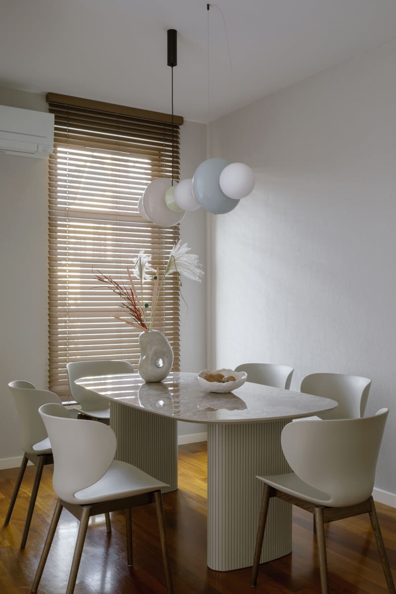 Oszczędną aranżację jadalni urozmaicają wyjątkowe formy wyposażenia: krzesła  z wyrazistą, wąską talią i stół z kamiennym wzorem na blacie z oferty BoConcept oraz wisząca lampa Aromas del Campo zbudowana ze szklanych kloszy w pastelowych barwach.