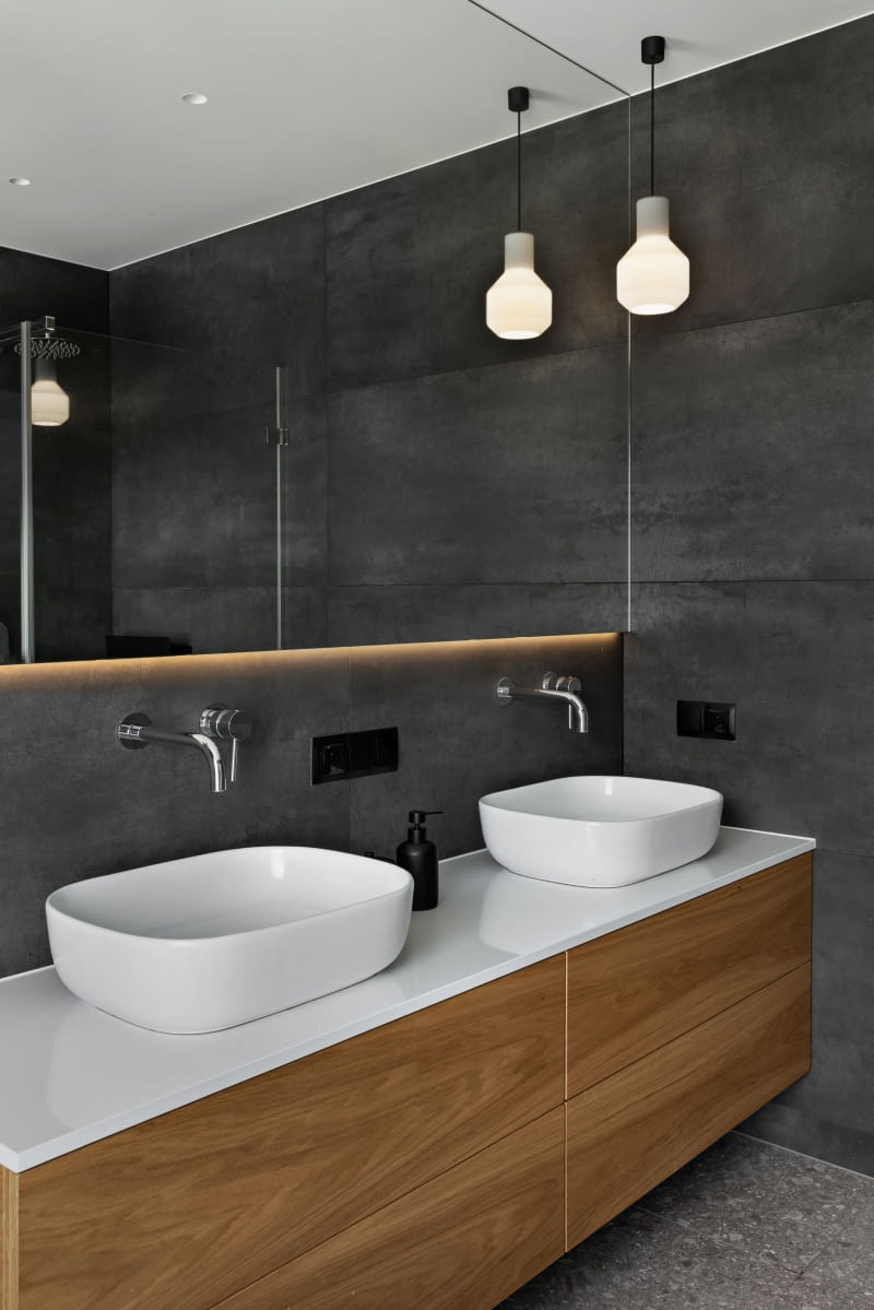 Ciemną łazienkę rozjaśnia duże lustro zamontowane nad umywalkami. Delikatnie odsunięta od ściany tafla szczególnie efektownie prezentuje się po włączeniu podświetlenia od spodu. Obok lustra zawieszono białe lampy AQForm Lighting. Wanna, umywalki i armatura pochodzą z salonów wnętrz Maxflitz. Ciemną łazienkę rozjaśnia duże lustro zamontowane nad umywalkami. Delikatnie odsunięta od ściany tafla szczególnie efektownie prezentuje się po włączeniu podświetlenia od spodu. Obok lustra zawieszono białe lampy AQForm Lighting. Wanna, umywalki i armatura pochodzą z salonów wnętrz Maxflitz.