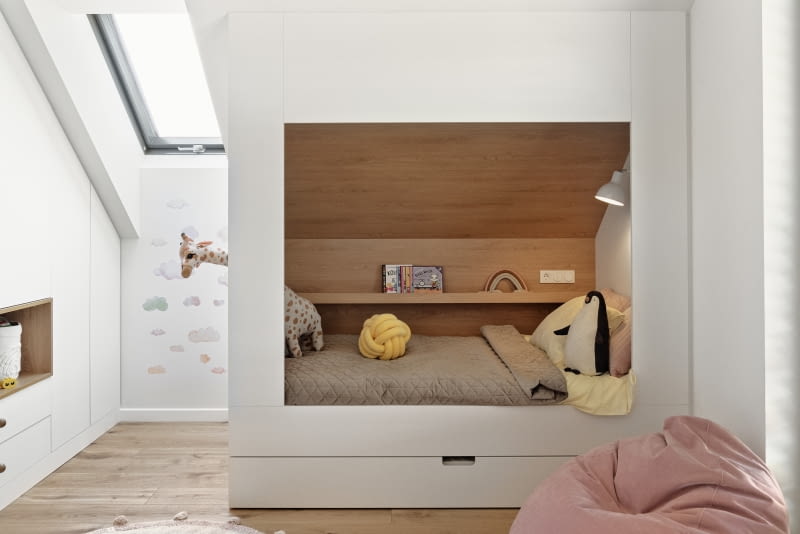 Łóżka-domki zaprojektowane przez architektów dla dzieci, oprócz materaca, wyposażono w środku w podręczną półkę, lampkę nocną, ukrytą skrzynię na skarby oraz wysuwany z dolnej części mebla dodatkowy materac potrzebny, kiedy na nocowanki zostają koleżanki. Stolarz wykonał domki z płyt laminowanych w bieli i w kolorze dębu.