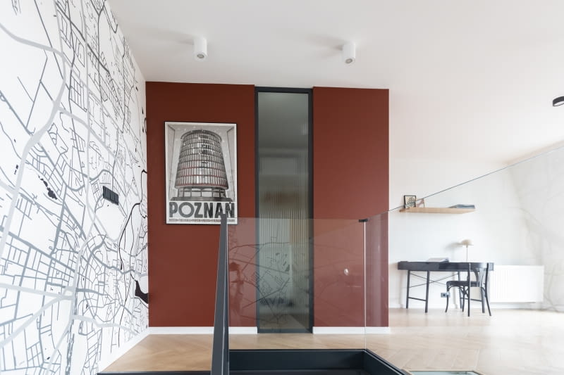 Wspinając się po schodach na piętro nie sposób zbagatelizować wrażenia, jakie robi bordowy kolor ścian wybudowanego tu, drugiego kubika. Napełnia wnętrze pozytywną energią i ciepłem. Wzrok przyciąga kolejny plakat artysty Ryszarda Kai. Przedstawia „Okrąglak” – modernistyczny budynek-symbol Poznania, który wywołuje u gospodarzy miłe wspomnienia z dzieciństwa. To waśnie bordowe przebłyski z grafiki zainspirowały projektantkę do użycia tej barwy w aranżacji całego mieszkania.