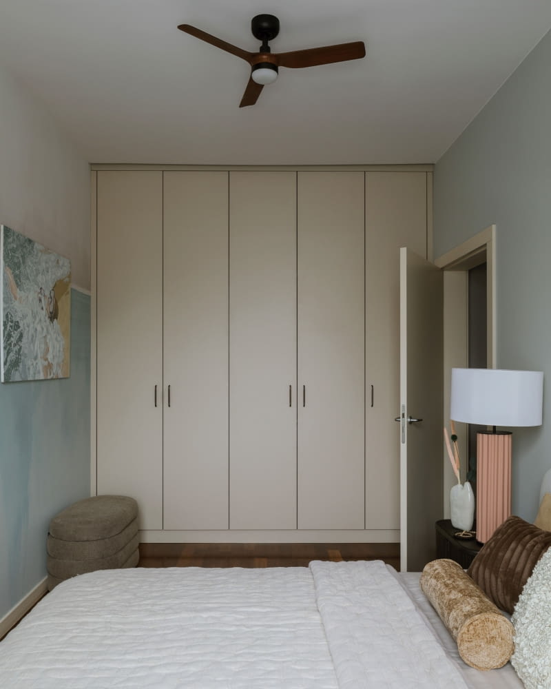 Przy krótszej ścianie sypialni stanęła rozpięta na całą wysokość sypialni szafa na ubrania. Stolarz wykonał jej fronty z MDF-u w kaszmirowym odcieniu.  Na suficie zainstalowano wiatrak z lampą Faro Barcelona, który chłodzi latem, a w zimne dni dogrzewa pomieszczenie.