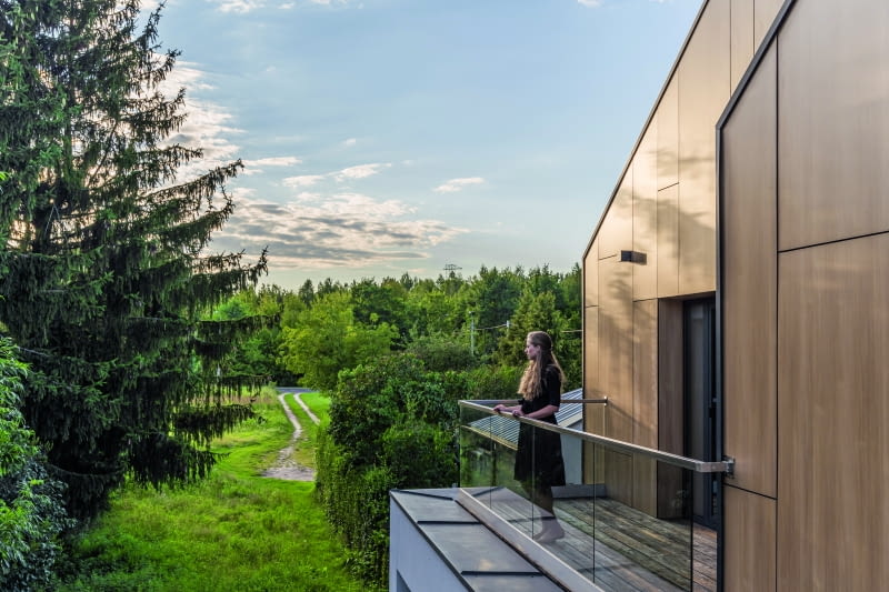 Po drugiej stronie domu horyzont zamykają widoki na zdecydowanie bardziej „suchą” przyrodę  niż od frontu – łąkę i ścianę drzew. Można je podziwiać z wąskiego balkonu przy sypialniach  córek