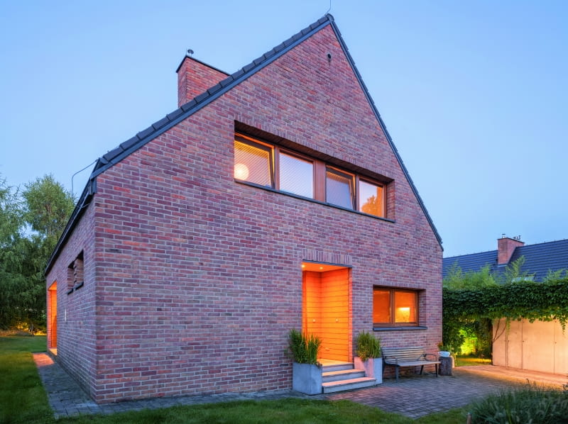 Dom w widoku od strony drogi dojazdowej. Uwagę zwraca wyraziste wycięcie w bryle budynku strefy wejścia głównego. Jakby na powitanie osoby wchodzącej przygotowano tam wizytówkę wnętrza – solidną dawkę dębowego drewna, którym dosłownie obłożono drzwi