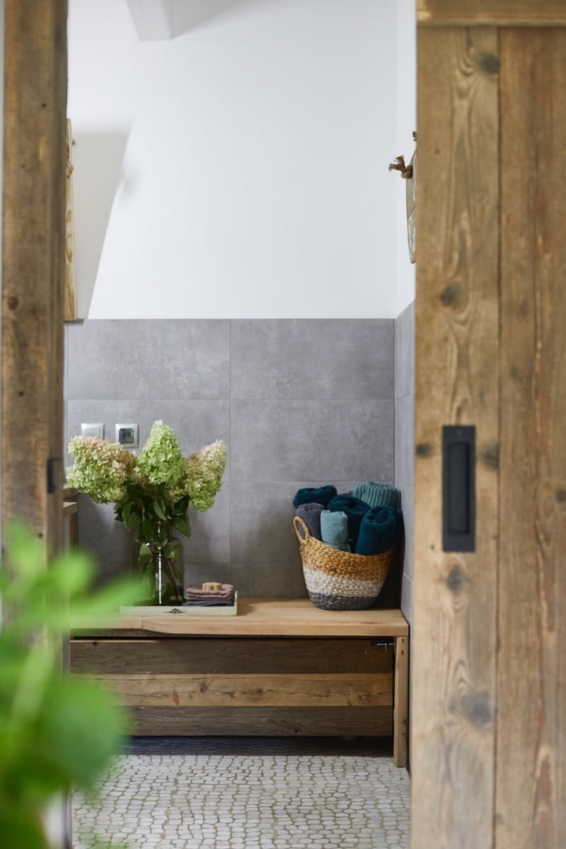 Z drewna powstały też drzwi do łazienki. Gospodarz wykonał je jako przesuwny, chowany w ścianie model. Tradycyjne, uchylne skrzydła kolidowałyby w tym miejscu z usytuowanymi obok drzwiami wejściowymi z wiatrołapu do strefy dziennej domu. Dodatkowo, kiedy drzwi do łazienki są zamknięte, ich piękne, drewniane deski stanowią urokliwą ozdobę strefy wejścia, idealnie wpisując się w rustykalny wystrój kuchni.