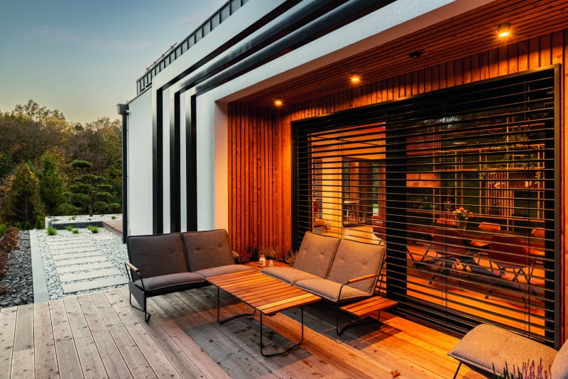 Po lewej stronie  od głównego wejścia, dokładnie  na wysokości  jadalni, powstał  mały taras, „przyklejony″ do niedużej  wnęki stworzonej  w bocznej elewacji, prawie  całej wyłożonej modrzewiem syberyjskim. Wykreowane w ten  sposób zadaszenie symbolicznie przedłużono ażurową  konstrukcją, nawiązującą do  formy ogrodowej  altany