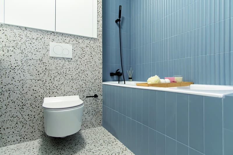 KRÓLESTWO PŁYTEK. Chodzi oczywiście o łazienkę. Tu nasza bohaterka razem z naszą projektantką wybrały na podłogę i ściany gładkie płytki heksagonalne Terrazo (to dobrze wszystkim znane lastryko, ale w nowoczesnej formie i odmianie). Natomiast w strefie kąpielowej znalazły się elementy 3D, tym razem w postaci płytek. Jasne, spokojne kolory plus modna tak ostatnio czarna armatura nadały wnętrzu elegancki, ponadczasowy charakter.