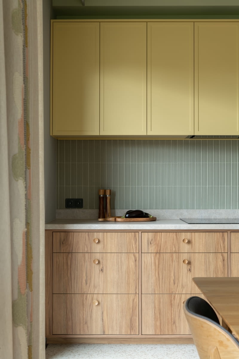 Estetyczny detal: uchwyty szafek wykonano w tym samym kolorze laminatu co ich fronty – to optycznie zespala je i podkreśla jednolitą linię zabudowy kuchennej. Nad blatem zielone, trójwymiarowe płytki Equipe Costa Nova Onda Tansy Green.
