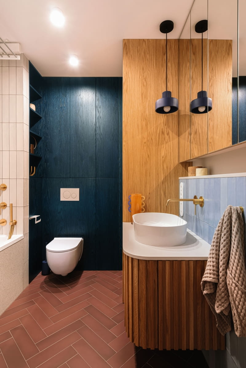 W łazience z wanną wiele elementów stolarz zrealizował według projektów architektek. Z bejcowanych na granatowo, fornirowanych płyt powstała elegancka zabudowa wokół stelaża WC, kryjącą praktyczne półki.