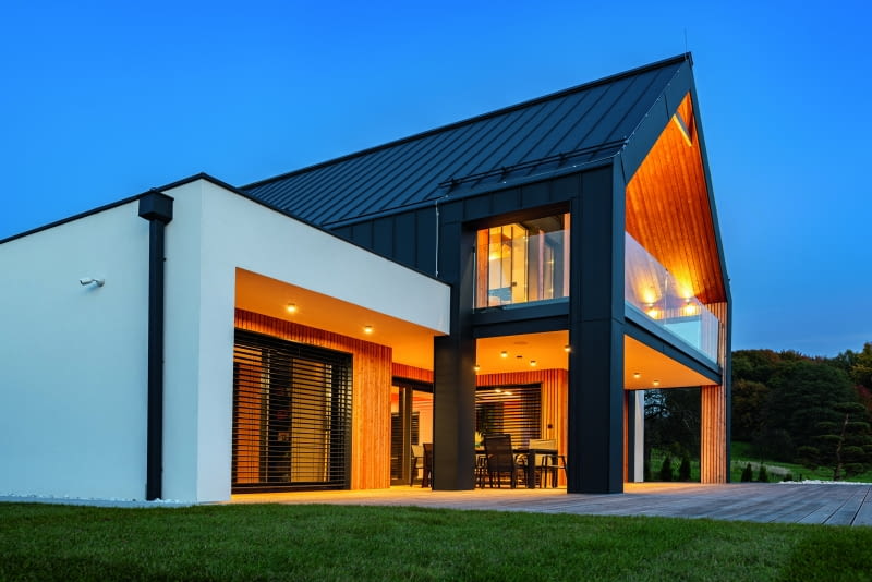 Cała realizacja złożona jest niejako z dwóch części – to trochę tak, jakby dwukondygnacyjną  nowoczesną stodołę, zawierającą część dzienną i prywatną, wstawiono w parterowy segment  z płaskim dachem, skrywający dwustanowiskowy garaż, schowek oraz otwarty widokowo  na ogród gabinet