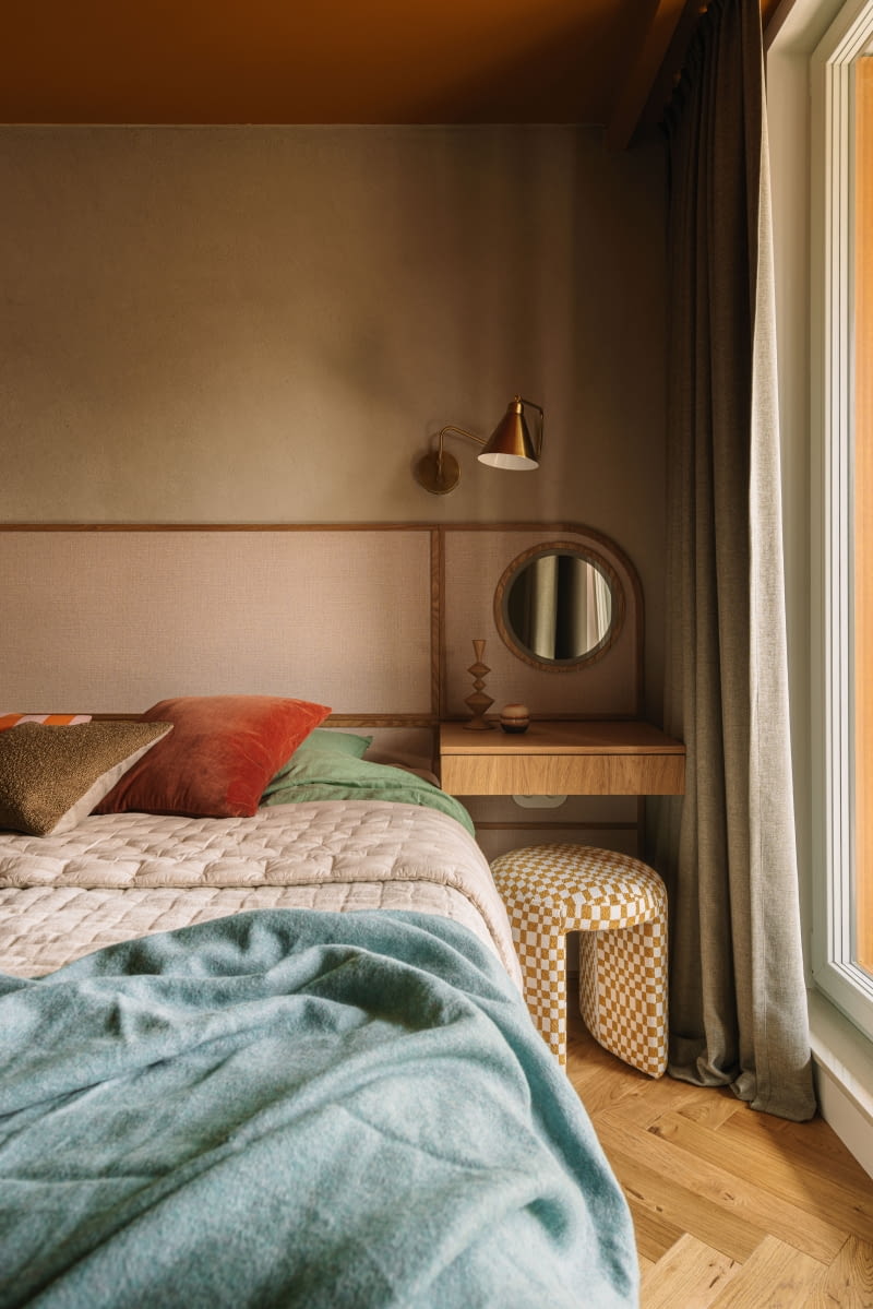 Centralnym punktem pokoju jest zabudowa z zagłówkiem zintegrowanym z toaletką. Zagłówek powstał z fornirowanych deseczek i tapety materiałowej. To użyteczne, ale również atrakcyjne wizualnie rozwiązanie tworzy kameralną atmosferę. Miły nastrój podkreśla też kilka innych akcentów: stołek obity tkaniną w żółtą kratkę marki Woood, ozdobna minirzeźba – totem z Totem Studio Warsaw, wazony HKliving, poduszki oraz narzuty z salonów NAP i Comforty.