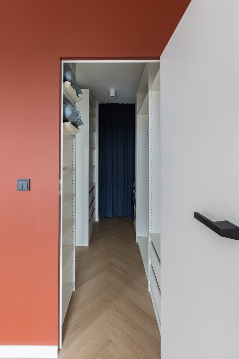 Druga strona bordowego kubika skrywa zlicowane ze ścianą drzwi z ukrytą ościeżnicą, elegancko wtapiające się w całą zabudowę. We wnętrzu oprócz półek na ubrania znalazło się małe pomieszczenie gospodarcze za zasłonką. Przewidziano tu też miejsce na pralkę. Przeniesione z łazienki na parterze urządzenie pozwoliło swobodniej rozporządzać jej ograniczoną przestrzenią.