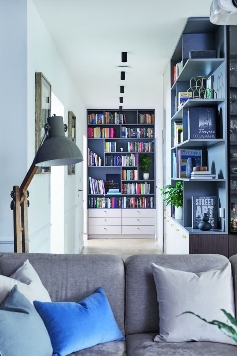 Regały na książki umieszczone w korytarzu akcentują ważne punkty w przestrzeni. Jeden widać zaraz po otwarciu drzwi wejściowych. Drugi umieszczono na końcu załamującego się korytarza. Takie usytuowanie optycznie skraca długi hol i dodaje mu innego, niż „przejściowy” charakteru. Ponadto stanowi ładne wykończenie ściany, którą widać z salonu.