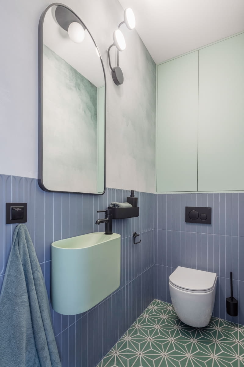 Wystrój toalety nawiązuje kolorystyką do barw użytych w salonie. Zielone oraz niebieskie płytki na ścianach i podłodze pochodzą od producenta Equipe Cerámicas. Ścianę z lustrem wykończono akwarelową fototapetą. Wystrój toalety nawiązuje kolorystyką do barw użytych w salonie. Zielone oraz niebieskie płytki na ścianach i podłodze pochodzą od producenta Equipe Cerámicas. Ścianę z lustrem wykończono akwarelową fototapetą.