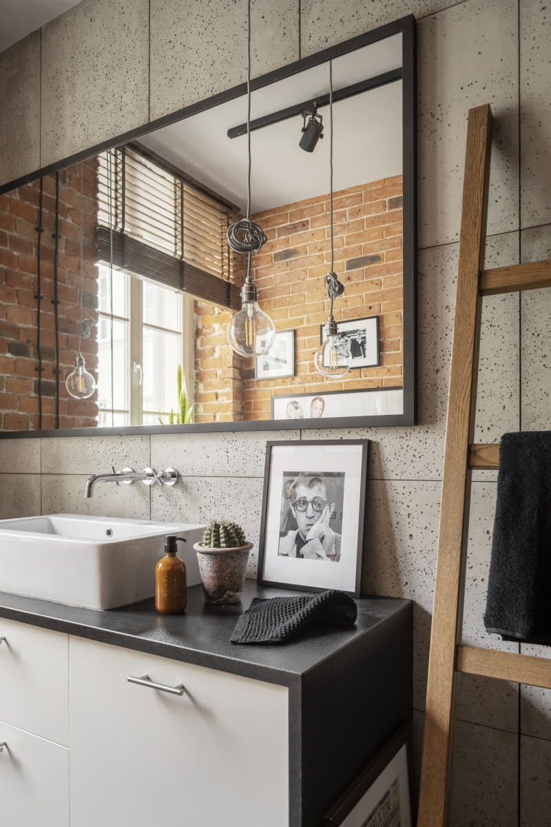 W loftowej łazience oprócz cegły i betonu nie mogło zabraknąć czerni oraz drewna. Klimat wnętrza podkreśla czarna, metalowa rama lustra, grzejnik, elementy oświetlenia oraz żaluzje w tym kolorze, a także szczotkowany, granitowy blat szafki umywalkowej. Drewniana drabina przejęła funkcję wieszaka na czarne ręczniki.