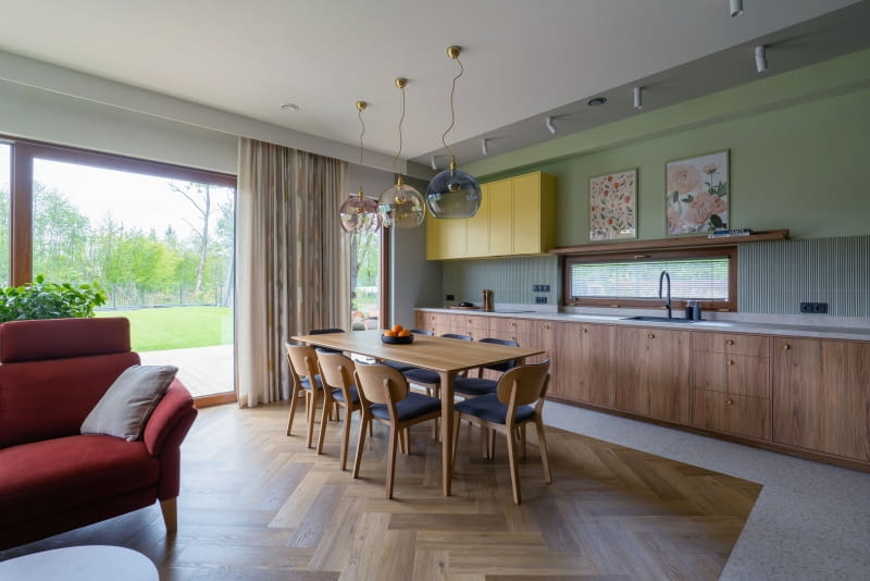 Kuchnię subtelnie wydzielono z otwartej strefy dziennej z pomocą różnych materiałów użytych na podłodze i suficie. Jasne, nakrapiane płytki marki Terrazzo, ułożone zgodnie z linią szafek, wyznaczają jej granice na posadzce, a na suficie odpowiada im wymalowany pas płaszczyzny w beżowoszarym kolorze. Dzięki temu kuchnia tworzy spójną, wyraźnie zarysowaną bryłę.