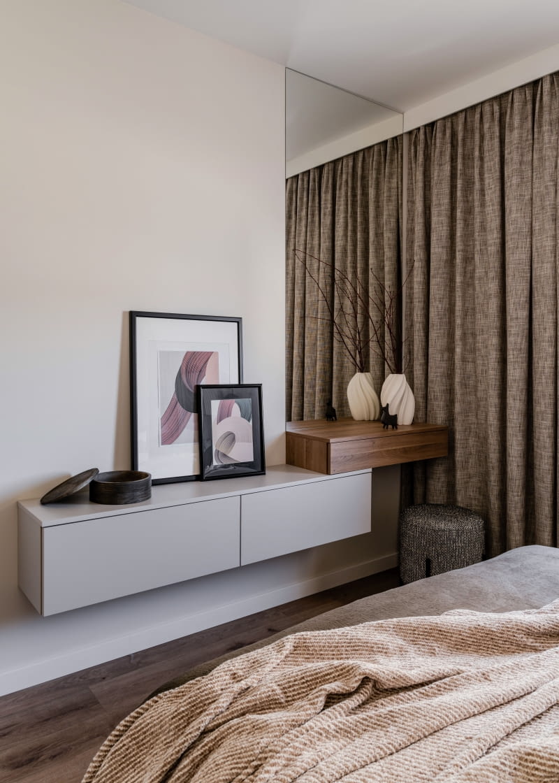 W sypialni wisząca, dwupoziomowa szafka powtarza wykorzystany w salonie i pokoju do pracy motyw poziomej półki, której  prosta bryła przecina  inną płaszczyznę - w tym przypadku lustro.  To ciekawy, rzeźbiarski zabieg, a jednocześnie funkcjonalna toaletka i miejsce na ekspozycję dekoracji.