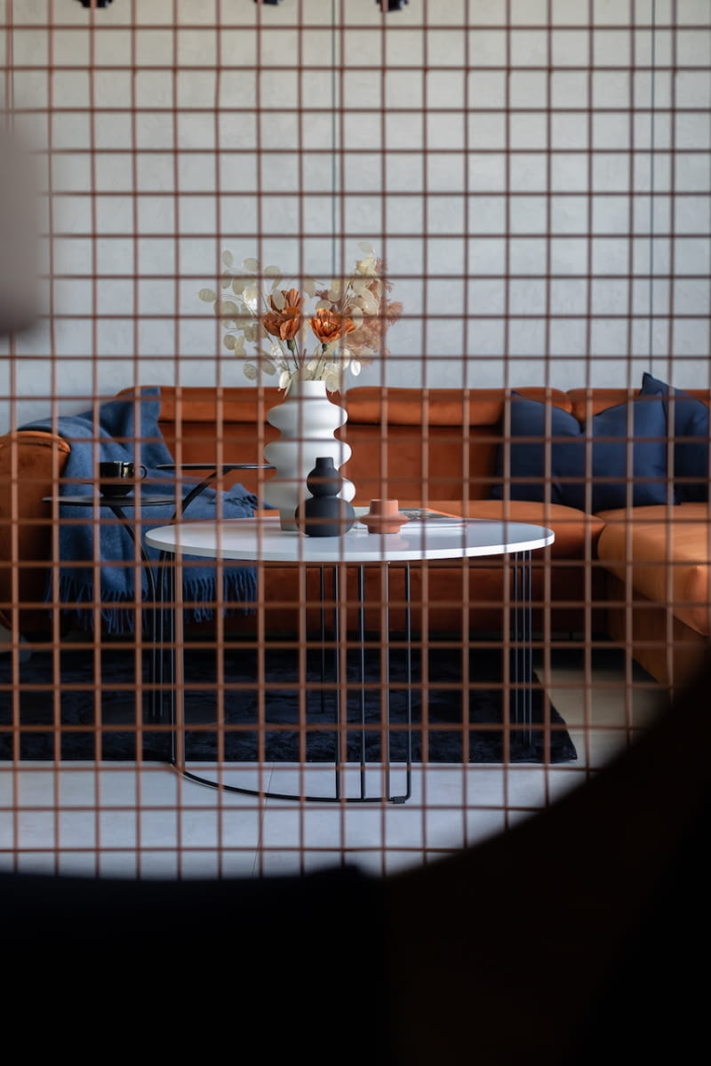 Stalowa siatka malowana w kolorze miedzi tworzy lekką przegrodę pomiędzy salonem, a jadalnią. Jest to ważny element dekoracyjny. Rudawa barwa współgra z odcieniem sofy i ramy wiszącego przy niej telewizora Samsung.