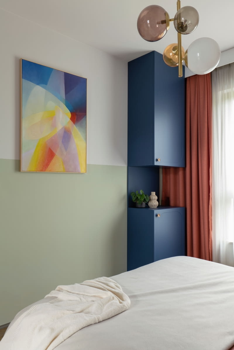 Wnętrze sypialni wzbogaca obraz autorstwa Macieja Kuleszy. Jest idealnie dopasowany kolorystycznie do aranżacji. Nad łóżkiem zawisła lampa ze szklanymi kloszami polskiego producenta Artea.