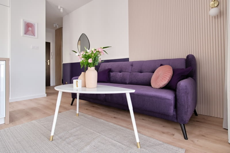 SALONOWA WYGODA. Przestrzeń salonu (i widocznego na zdjęciu obok aneksu kuchennego ) jest utrzymana – zgodnie z życzeniem Dominiki – w jasnych barwach. Przełamują ją mocna kolorystycznie, wygodna sofa – obowiązkowy element tego pomieszczenia, a także lamperia i oryginalne, ozdobne panele 3D (Agnieszka postanowiła pomalować je na beżowo). Uzupełnieniem aranżacji jest niewielki, zgrabny stolik oraz miękki dywan.