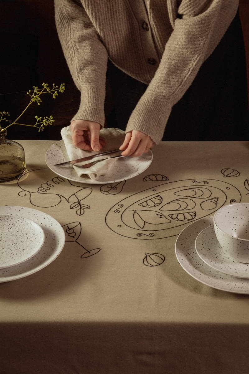 „Rysowane” owocowe i warzywne wzory na obrusie ożywiają stół utrzymany w stonowanych kolorach.