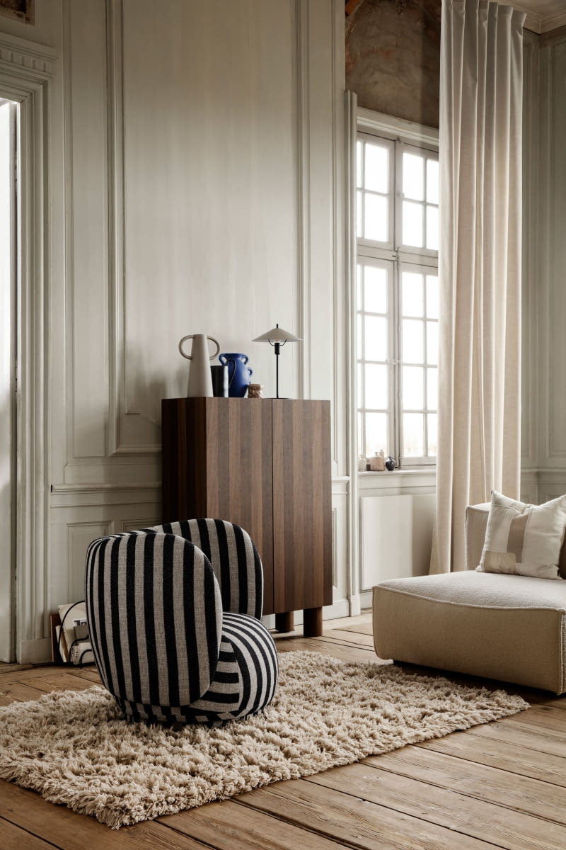 Obła, rzeźbiarska forma i otulająca sylwetka fotela Rico Lounge Chair (Ferm Living) przełamuje proste linie klasycznych paneli ściennych.