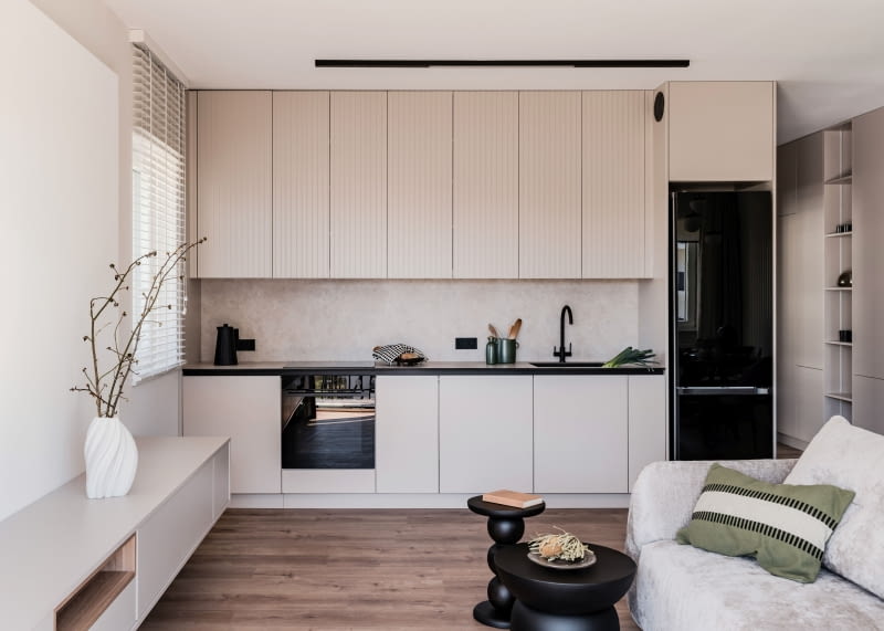 W zabudowie kuchennej zestawiono dwa kolory: kaszmirowe fronty i blat przełamano czarnymi dodatkami, które dodają całości głębi i nowoczesnego wyrazu.