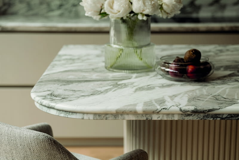 W kuchni detale, takie jak zaokrąglony marmurowy blat wyspy kuchennej, tworzą sprytną grę symetrii i asymetrii. Tara Ultra w kolorze Brushed Dark Platinum doskonale komponuje się z ciemnobrązowymi frontami kuchni.