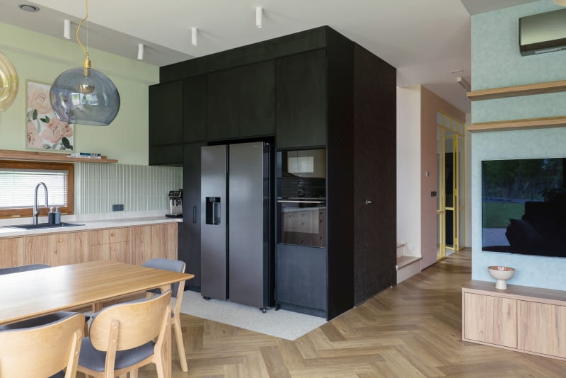 Najmocniejszym akcentem kuchni jest czarny kubik, który mieści sprzęty AGD i pojemne szafki. Prostopadle do jego bryły biegnie ciąg dolnych szafek.