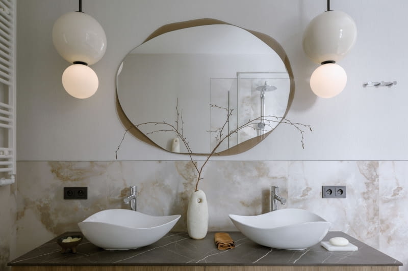 Szczególnie ciekawie prezentuje się aranżacja wokół szafki umywalkowej. Do wysokości narażonej na chlapanie wody ścianę chroni gres producenta Tubądzin, a powyżej tapeta o splocie tkaniny. Umywalki Ohtake Roca i lustro Osmo z GieraDesign  o organicznych kształtach zestawiono z wiszącymi lampami- -kulami z tej samej kolekcji Aromas del Campo co lampa w jadalni.