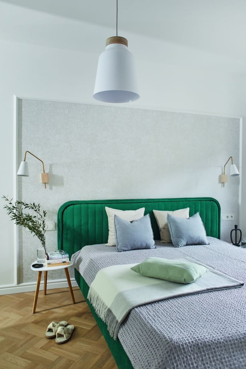 Zielone, tapicerowane łóżko od Scadicsofa wprowadza do jasnej sypialni pozytywną energię. Jego wezgłowie podkreśla specjalnie zaaranżowana ściana, ujęta w ozdobne listwy. Wyznaczony fragment muru wykończono przy użyciu tapety w odcieniach ciepłej szarości. Tekstylia: poduszki, kapa, pledy pochodzą z @yourest_studio.