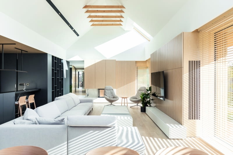 Prawie cały parterowy budynek ustawiony na samym szczycie góry wypełnia połączona przestrzeń salonu z jadalnią (niewidoczną, bo z niej zrobiono  zdjęcie) oraz kuchnią (po lewej). Wrażenie dużej kubatury podkreśla odsłonięcie połaci dachowych z konstrukcją więźby oraz światło wpadające przez  wielkie okna i odbijające się od jasnych powierzchni mebli, ścian z fornirów dębowych i podłóg z dębowych desek