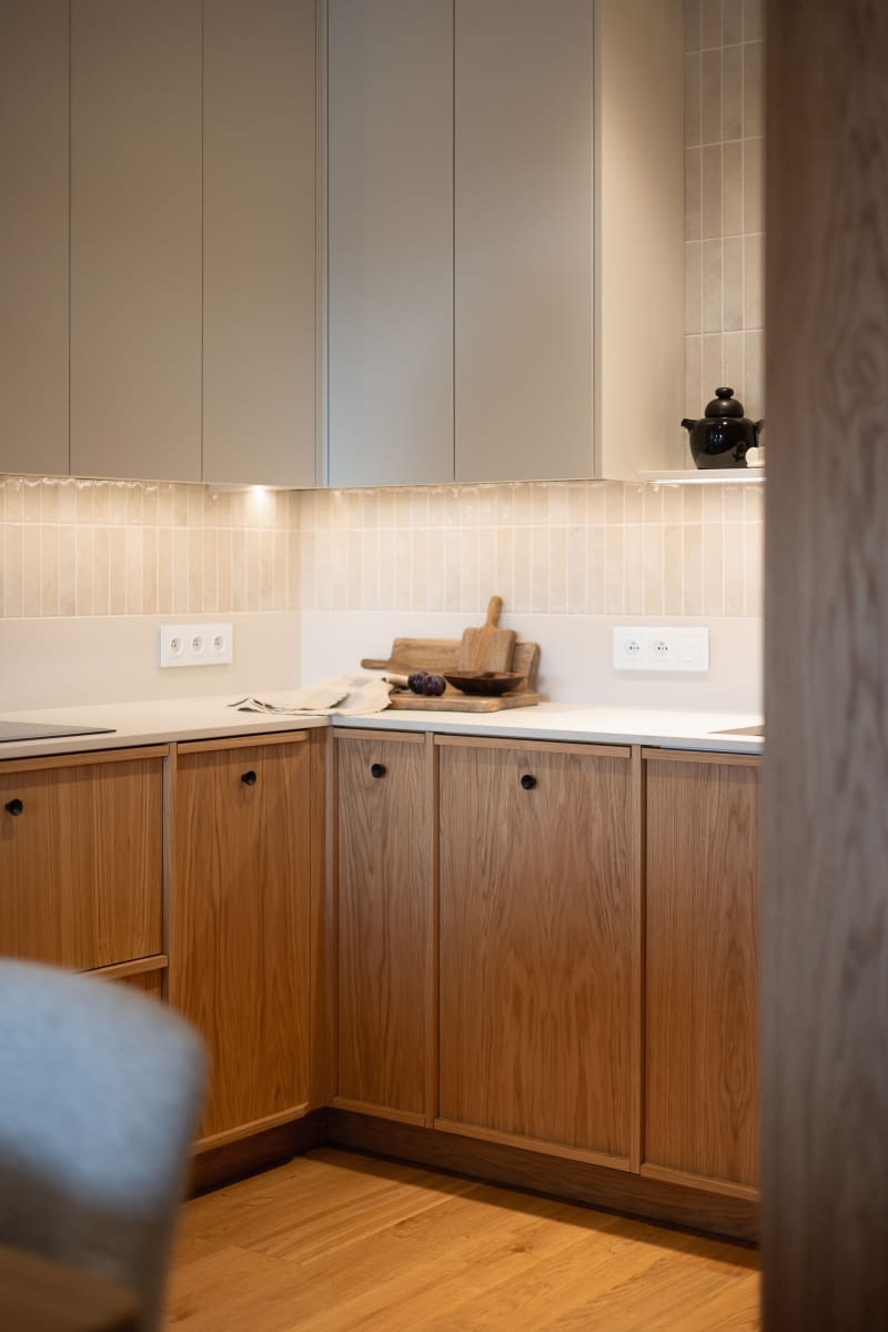 Dolny rząd szafek wykończono dębowym fornirem z dekoracyjną ramką, podczas gdy w wysokiej zabudowie fronty pozostawiono gładkie, aby uspokoić ich dużą płaszczyznę. Blat ze spieku kwarcowego Dekton Cosentino, inspirowany białym wapieniem, łączy kremowe i białe tony. Duet drewna i jasnego „kamienia” buduje spokojny, harmonijny wystrój.