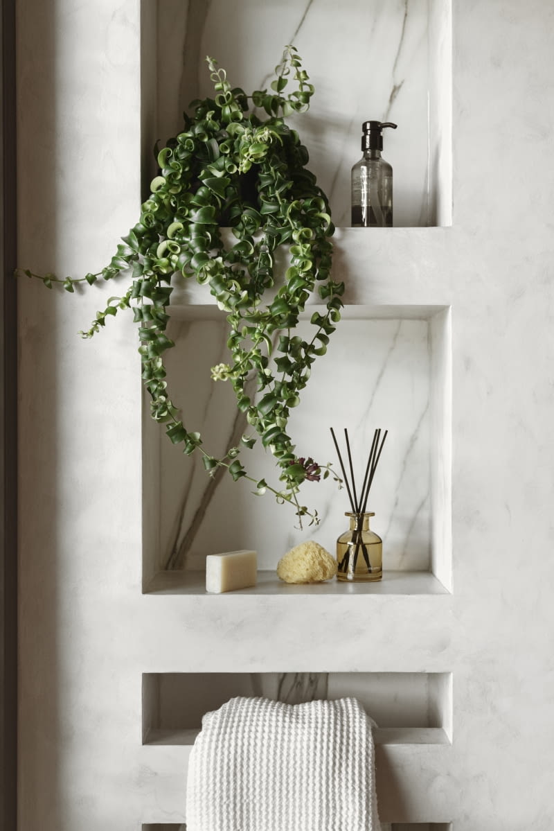 Obok szafki umywalkowej, w strefie zaplanowanego tu prysznica wybudowano wnękę na kosmetyki z półkami. Jest też reling na ręcznik, po który można sięgnąć na koniec kąpieli. Półki wykończono tak jak ściany i podłogę łazienki, z użyciem tej samej żywicy i gresu.