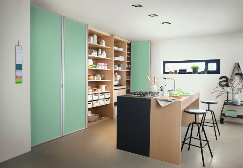 W tej kuchni za składanymi drzwiami postanowiono ukryć jedynie strefę do przechowywania – blat roboczy, płytę grzewczą i zlewozmywak umieszczono na wyspie.