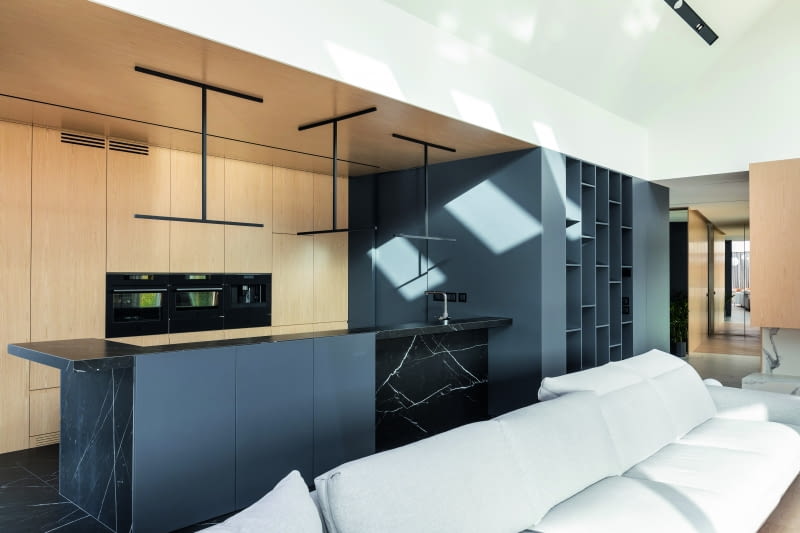 Elewacyjną grę kolorystyczną między jasnym brązem a ciemnymi barwami odnajdujemy też w kuchni, w której fornir płyt MDF wokół piekarników zestawiono z czernią lakierowanych płyt MDF kubika kryjącego pomocniczą ku