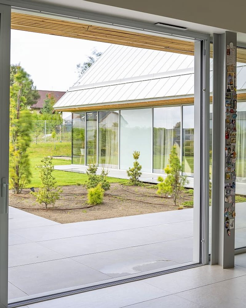 Wysokiej klasy aluminiowa stolarka okienna zatrzymuje ciepło, a wielkość przeszkleń  „robi” resztę: doprowadza naturalne światło do wnętrz i umiejętnym kadrowaniem ogrodu zaciera granicę między domem a otoczeniem