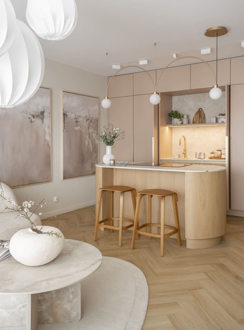 Dekoracyjna lampa o mlecznych kloszach zawieszona nad wyspą kuchenną daje przyjemne, delikatne światło podczas posiłków.