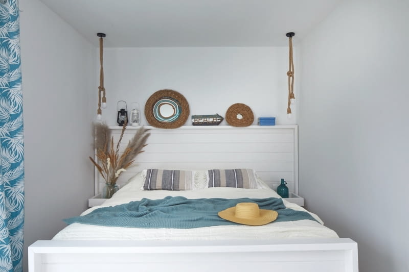 W sypialni rodziców bazę kolorystyczną, tak jak w całym domu, stanowi biały kolor i drewno. W wąskim pomieszczeniu zaplanowano na wymiar łóżko z zagłówkiem i zamocowanymi do niego półkami. Wykonał je oczywiście Szymon.