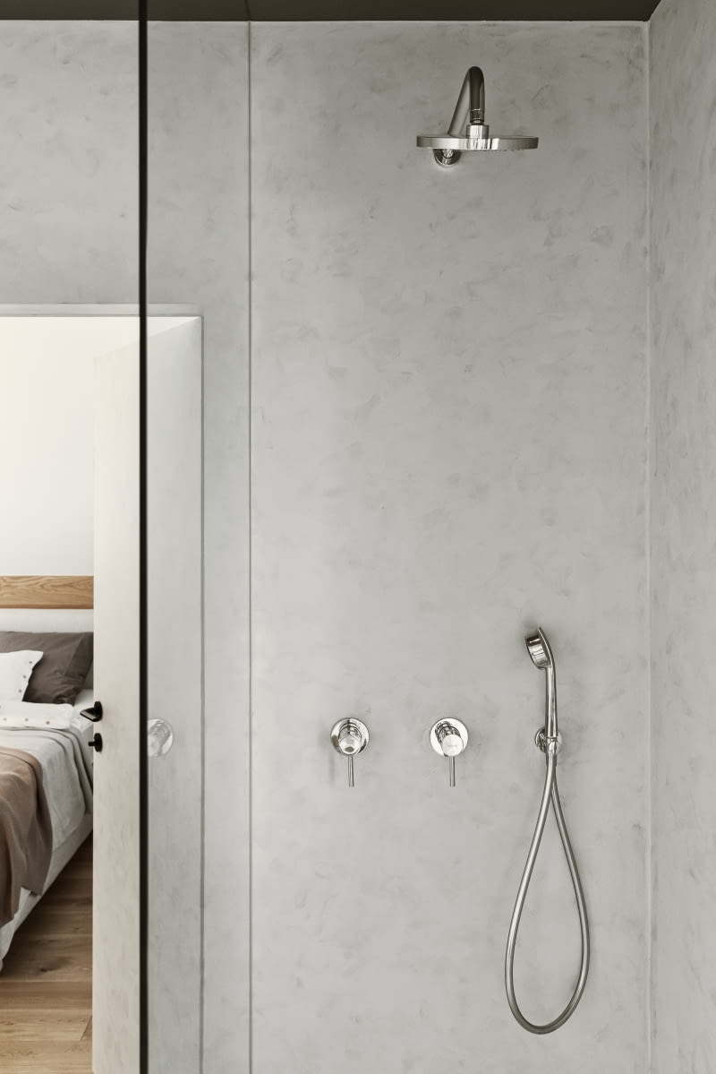 Ściany w łazience, jak również w strefie prysznica, wykończono jasnoszarą żywicą, a podłogę gresem marki Emil Ceramica, naśladującym kamień o szarym użyleniu. Do wszystkich łazienek dobrano baterie w kolorze chromu, harmonijnie wpisującego się w kolorystykę aranżacji, w których przeważają szarości. Jak podkreślają architekci, chromowane baterie są ponadczasowe, a na tym aspekcie zależało właścicielom.