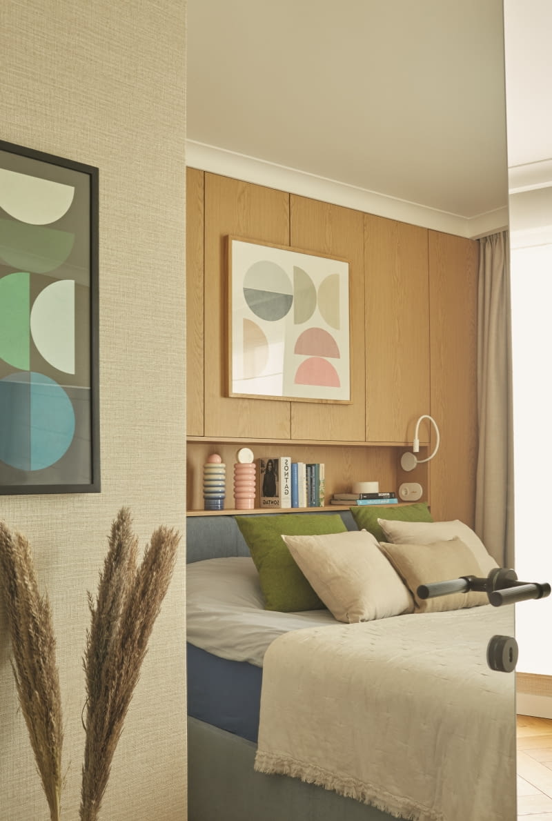 W lustrzanej powierzchni uchylonych drzwi do sypialni rodziców można podejrzeć widok ze środka pokoju. Po intensywnych doznaniach wizualnych strefy dziennej sypialnia przynosi ukojenie zmysłów. Królują tu stonowane, ciepłe barwy. Ściany zdobi tapeta ze wzorem plecionego płótna. Wszystkie tkaninowe dodatki wykonała firma Moniki Czypionki z Ach!Dom w Katowicach. Pastelowe obrazy namalował Piotr Kuchciński. Podobnie jak poduszki i kapę zdobiące łóżko, można je kupić w Noti Studio.