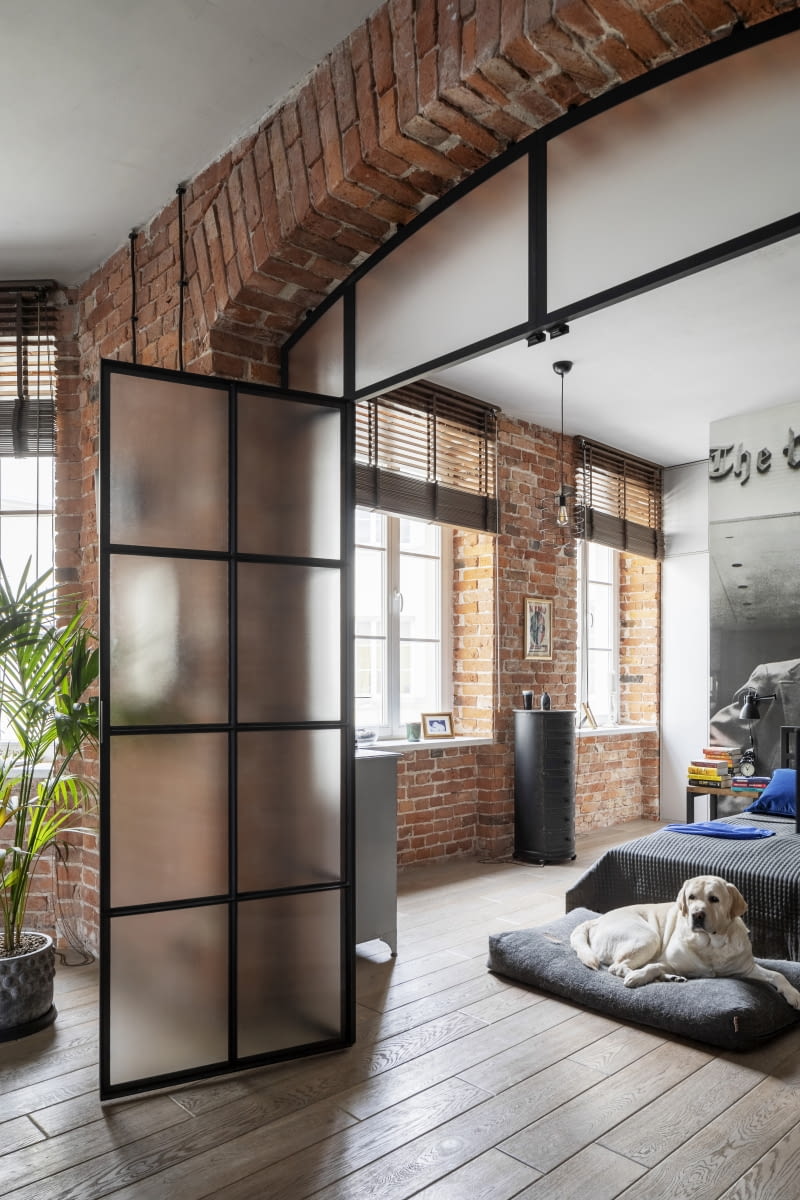 Autentyczny charakter dawnej, praskiej kamienicy z fabryczną historią w tle podkreśla ceglana ściana z łukowym przejściem pomiędzy salonem a sypialnią. Na jego osi, w głębi traktu znalazł się kadr z filmu Alana J. Pakuli „Wszyscy ludzie prezydenta” z niezapomnianymi rolami Dustina Hoffmana i Roberta Redforda. Nie lada wyzwaniem dla wykonawców (spawaniewarszawa.pl) było wpasowanie w łuk metalowych profili drzwi.