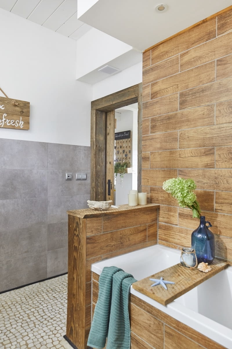 Wyrazistym akcentem łazienki są naturalne materiały wykończeniowe – kamyki na posadzce i surowe deski, z których Szymon zrobił szafkę umywalkową, skrzynię do siedzenia oraz ramę lustra. Nadają wnętrzu miły, prosty charakter.