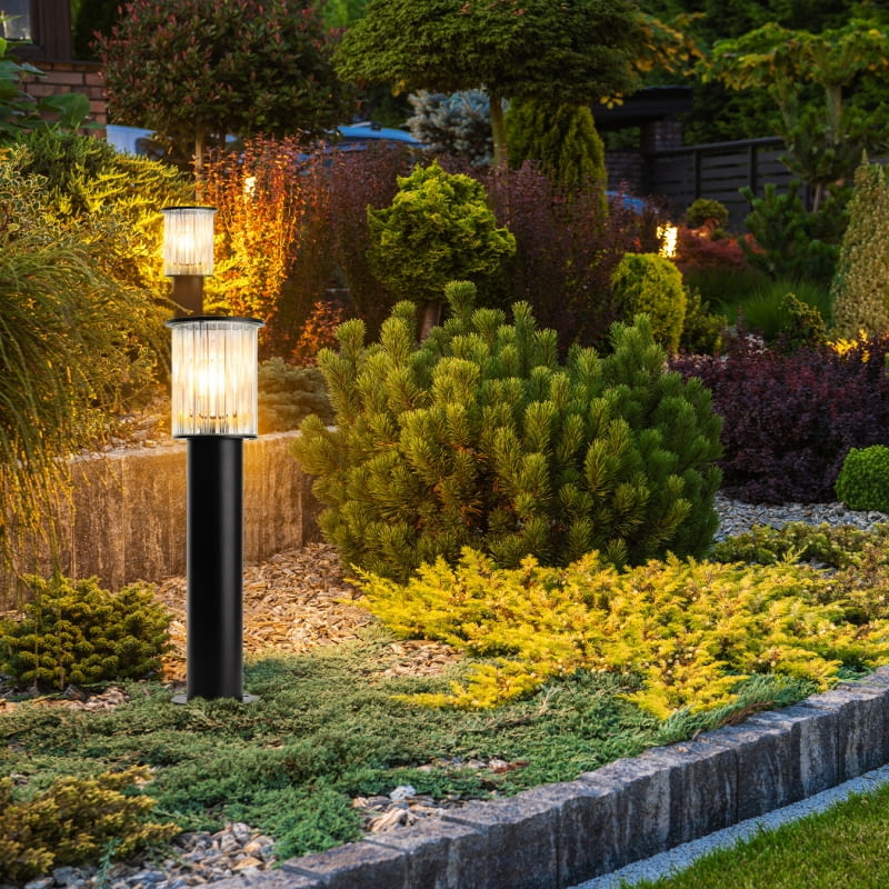 Lampy Norfolk umieszczone w rabacie oświetlają rośliny, tworząc dekorację po zmierzchu.