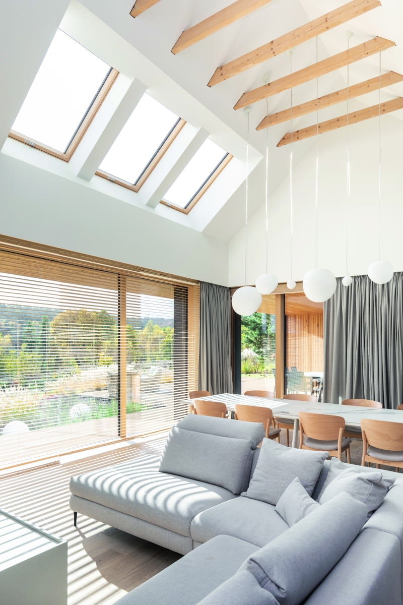 Długi stół  jadalni umieszczony  za salonową sofą  tonie za dnia  w świetle  słonecznym,  napływającym  zza wielkich okien  i przeszkleń  dachowych, a po zmroku  oddaje się we władanie  kulistych lamp,  zwieszających się  spomiędzy belek  więźby.  Za nim,  w głęboko  zadaszonym  tarasie, usytuowano drugi  salon, letni – z obu  roztaczają się  wspaniałe widoki  na całą okolicę